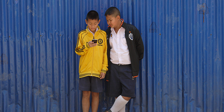 School kids access a smartphone while waiting for class to start. Photo credit: ADB